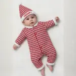 Baby wearing a red and white Christmas houndstooth jumpsuit with fur trim and a festive personalized Santa cap.